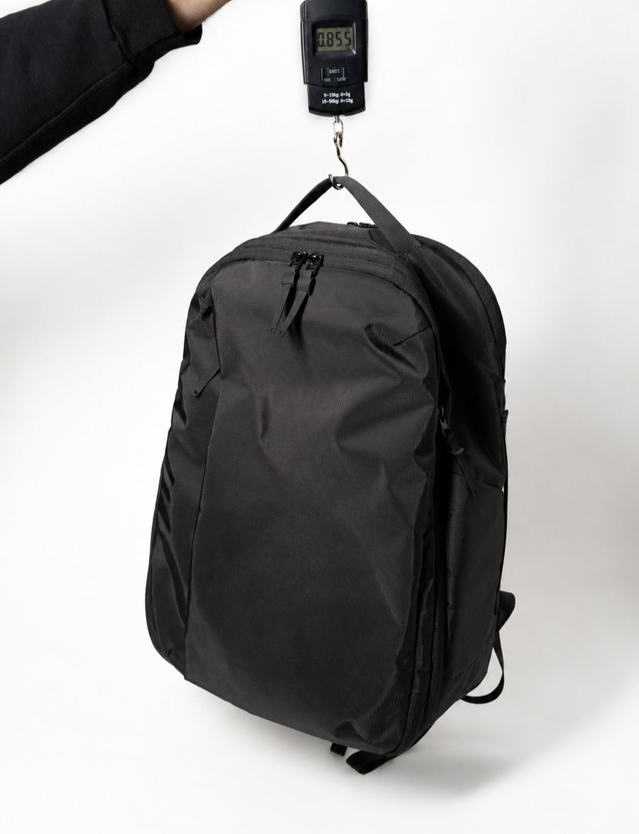 Almond Oak backpack hanging from a digital luggage scale reading 0.855kg